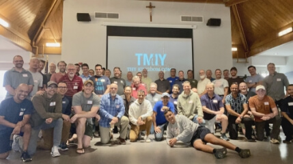 Group of TMIY particpants smiling for the camera in front of screen showing the TMIY logo.