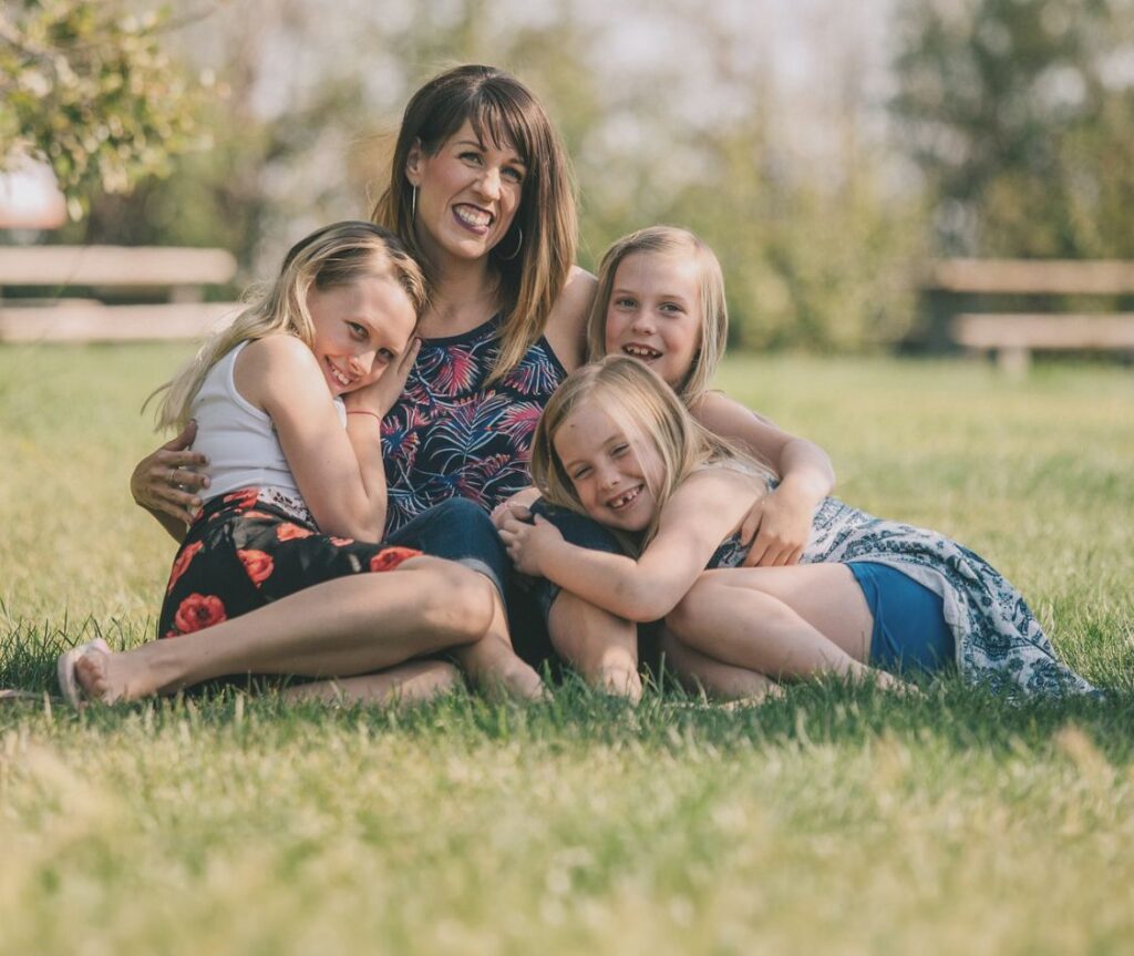 Mother and three young daughters sitting on the grass and hugging.