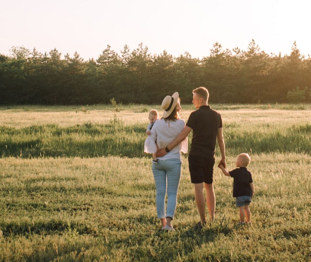 Young husband and wife and their two small children in a field.