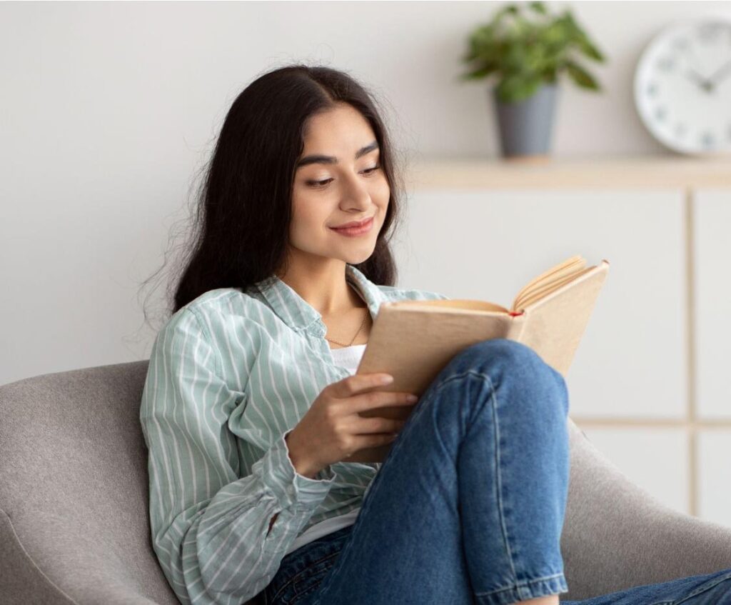 Young woman reading a book in a chair in the living room.
