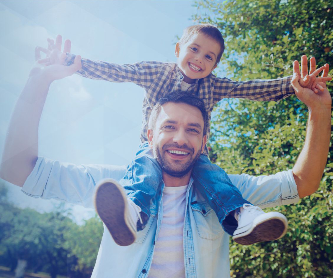 Young smiling father carrying young smiling boy on his shoulders outside.